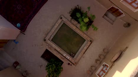 birds eye shot, traditional historical mud brick house in a desert village with a small pool and fig tree inside architecture, wooden doors and windows ruins during earthquake in tabas, esfahak, iran