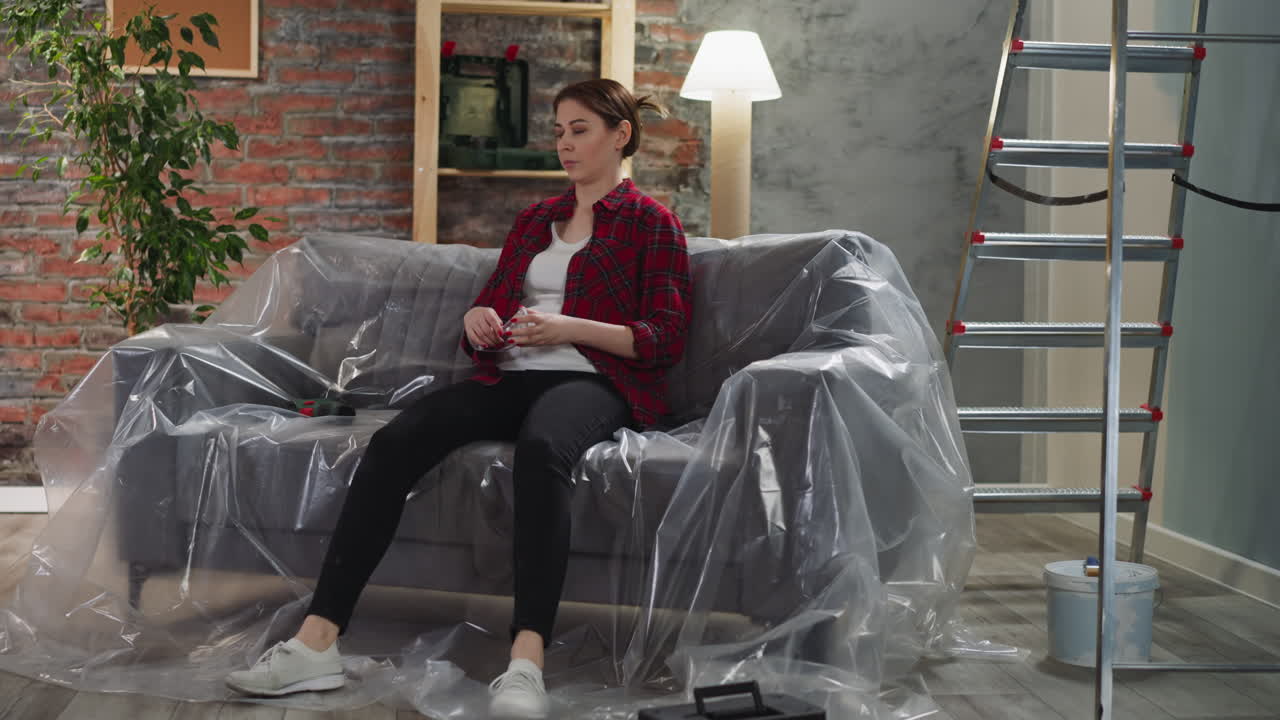 Tired woman with goggles and drill falls onto sofa at home