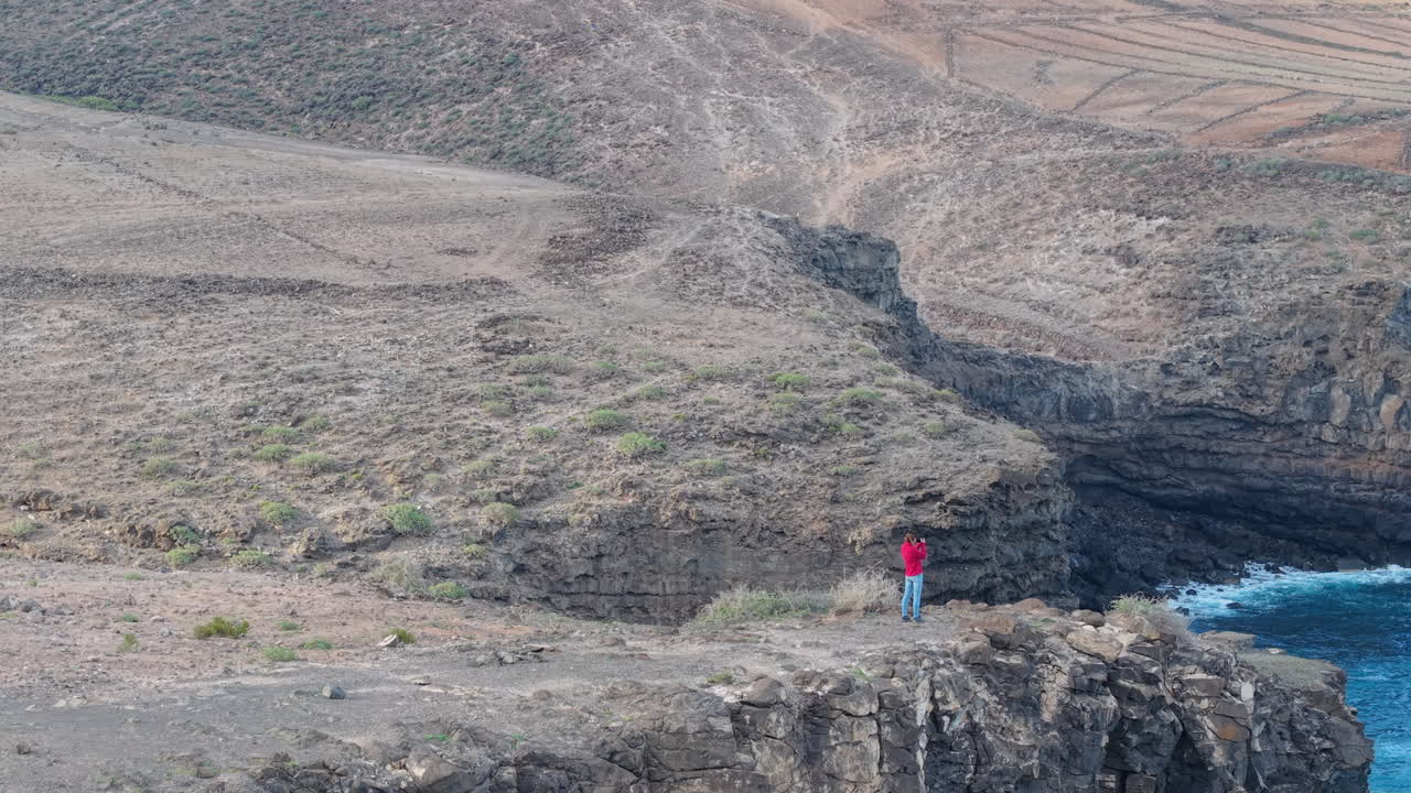 Woman photographing the atlantic ocean from a cliff near of Roque Partido, Gran Canaria