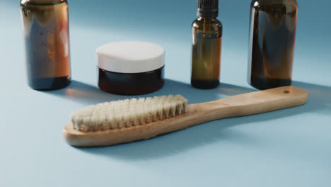 Close-up-of-glass-bottles,-cream-tub-and-brush-with-copy-space-on-blue-background