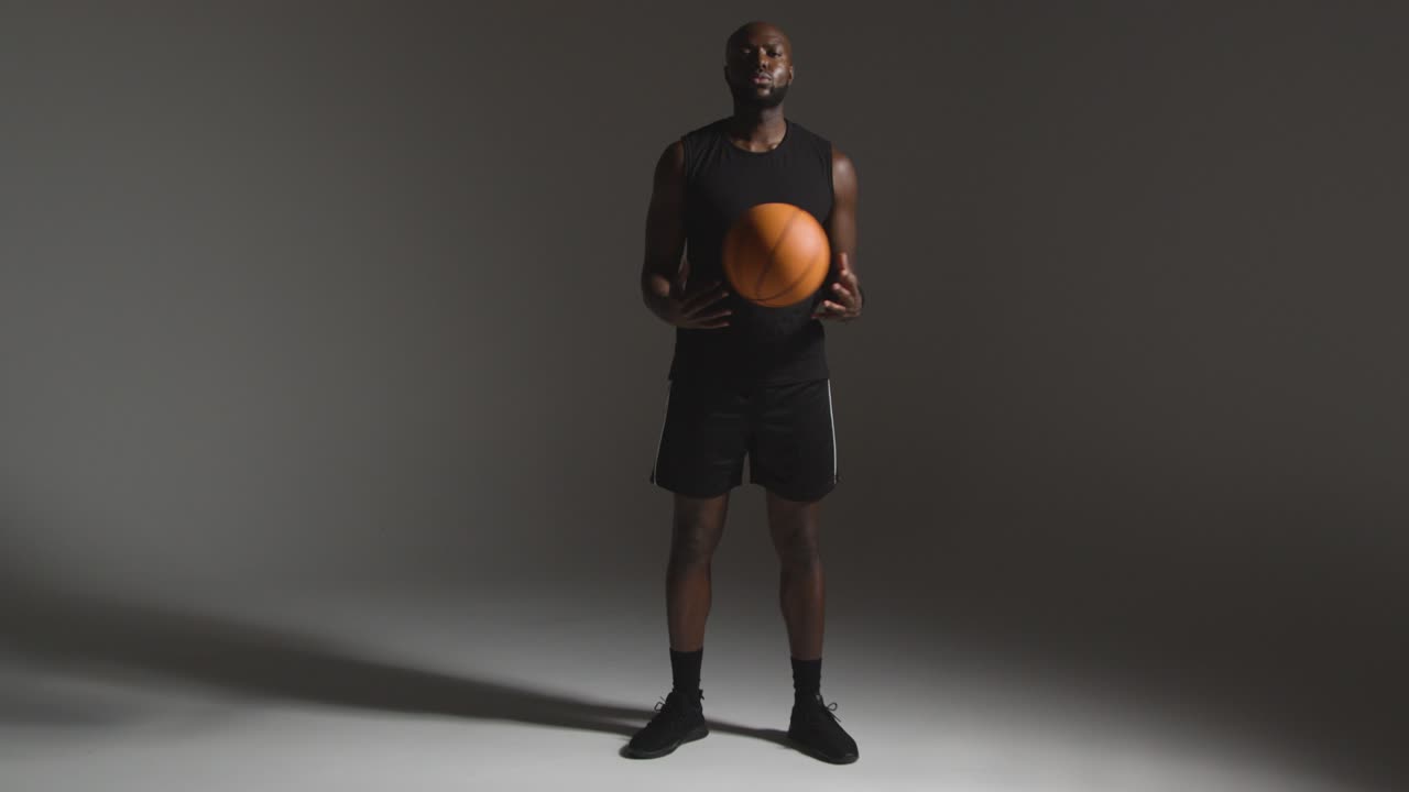 retrato de estudio de longitud completa de un jugador de baloncesto masculino lanzando la pelota de mano en mano contra un fondo oscuro
