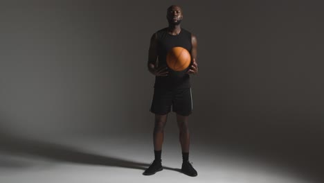 Studioporträt-In-Voller-Länge-Eines-Männlichen-Basketballspielers,-Der-Vor-Dunklem-Hintergrund-Den-Ball-Von-Hand-Zu-Hand-Wirft