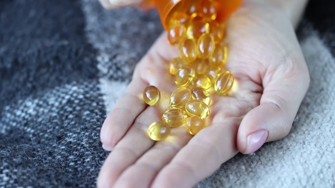 Yellow gel capsules being poured from a bottle into a hand