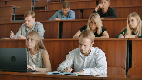 Los-Estudiantes-Modernos,-Hombres-Y-Mujeres,-Se-Sientan-En-Escritorios-En-Un-Aula-Grande-Y-Escriben-Notas-De-Clase.-Obtener-Una-Educación-Para-Una-Carrera-Exitosa