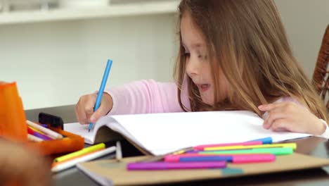 little girl drawing at the kitchen table and smiling at camera