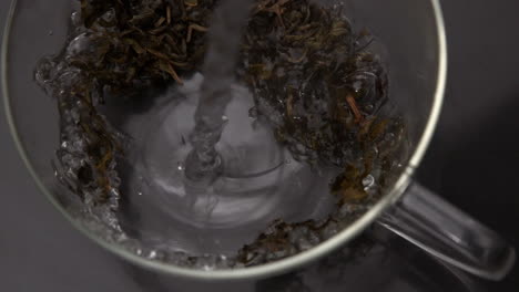 water pouring over loose herbal tea in glass cup