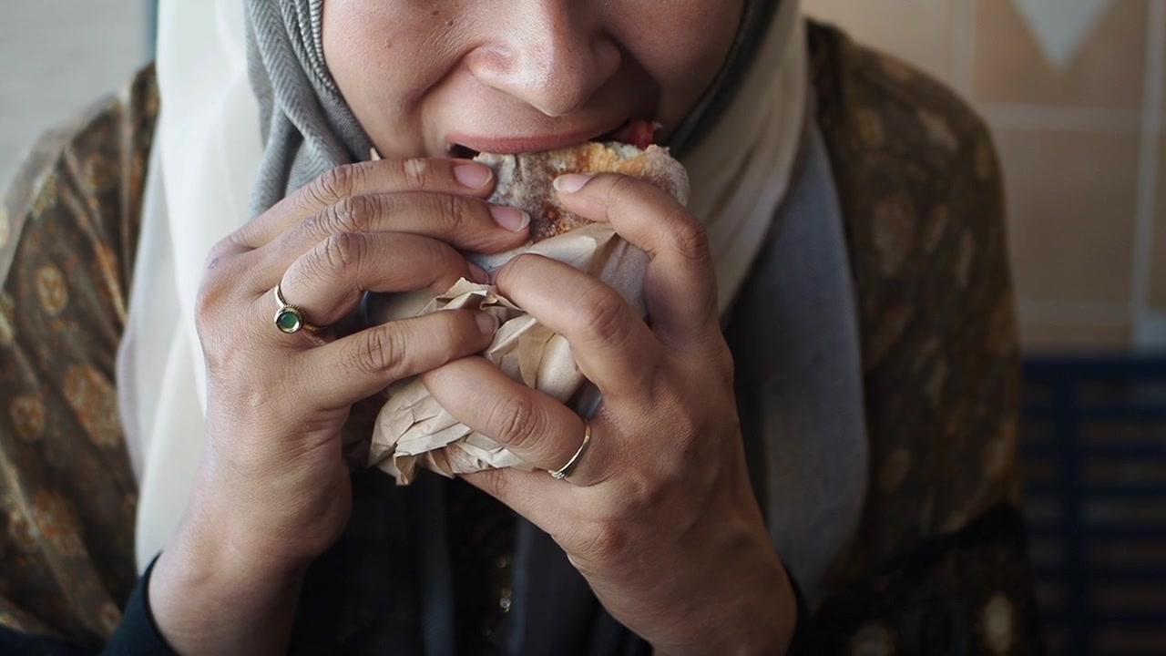 Kvinde med hijab spiser en sandwich på en café