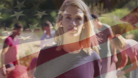 composite video of american flag over portrait of caucasian female volunteer smiling in the forest