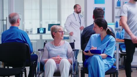 nurse filling documents while talking with disabled senior woman