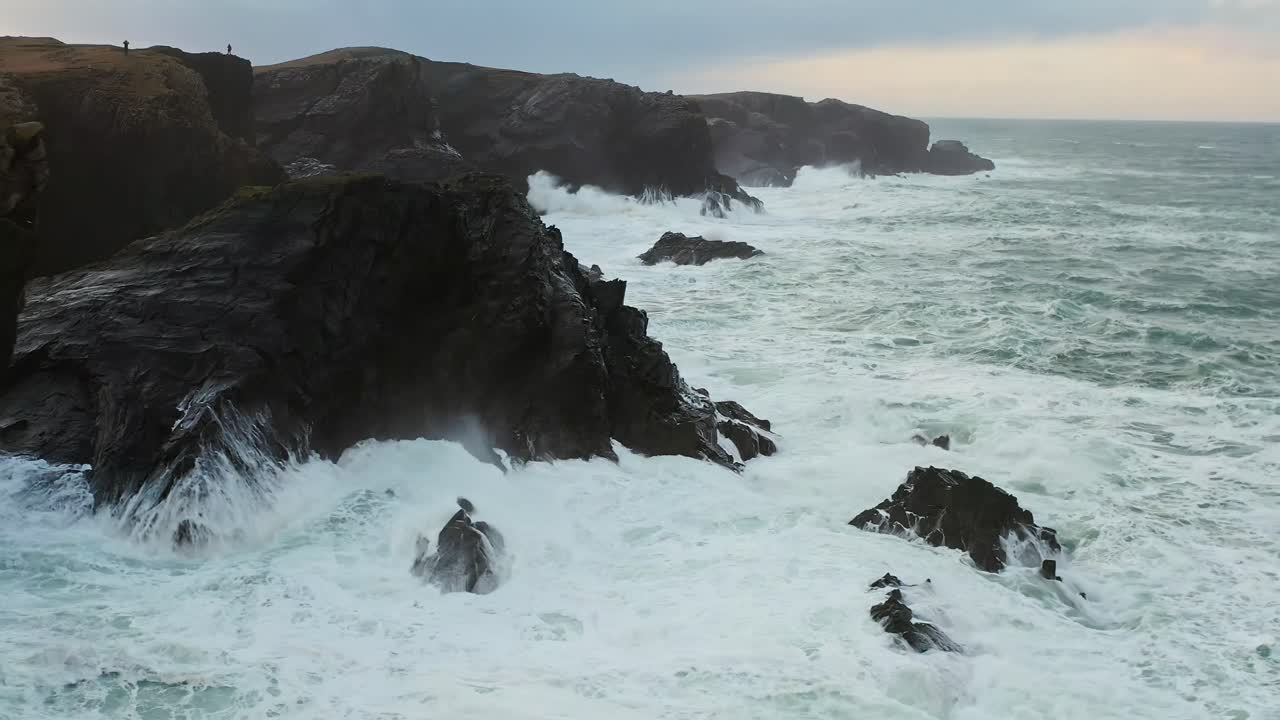 Drone shot of roiling waves breaking against a Hebridean cliffside
