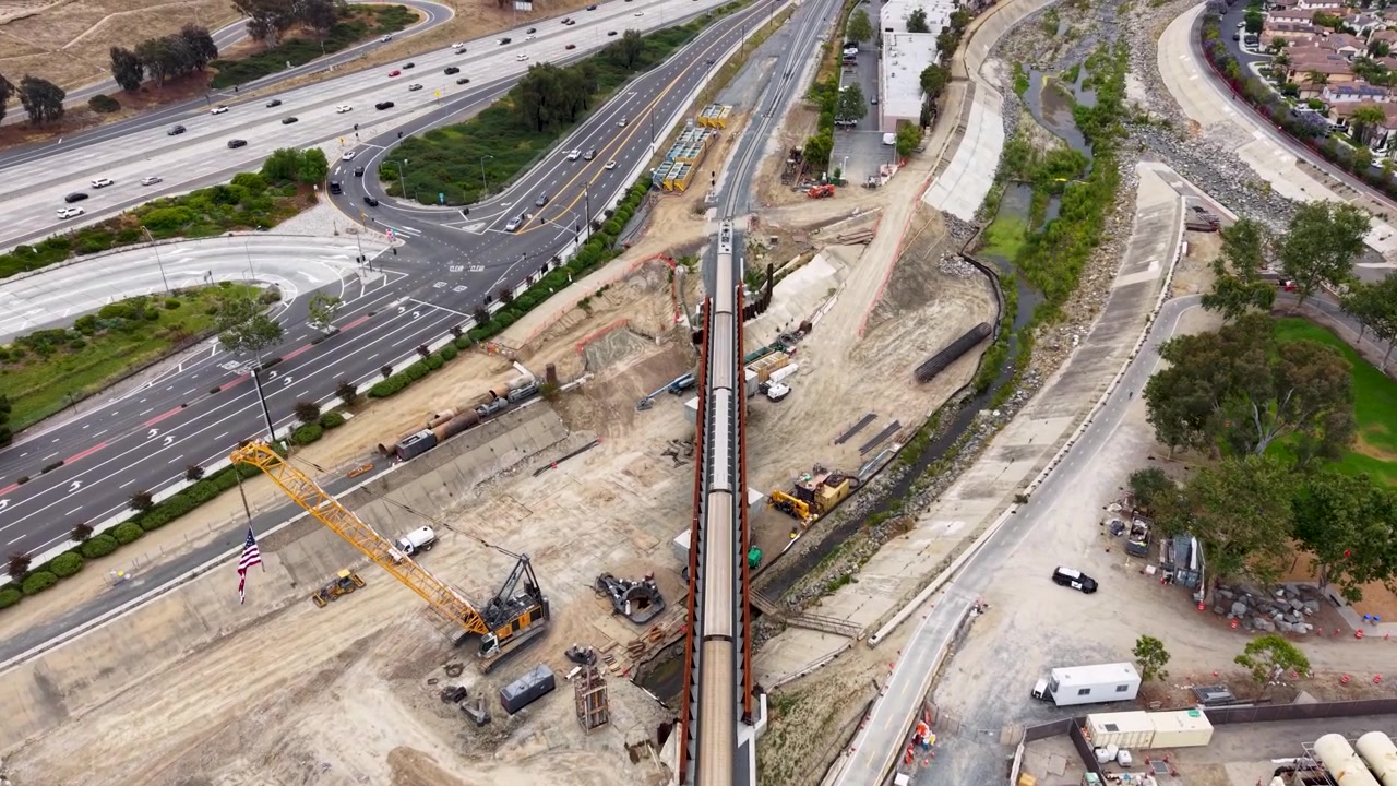 Vista aérea cinematográfica de un tren saliendo de San Juan Capistrano en dirección a San Diego. La toma utiliza un dron con cámara 4k para capturar una vista descendente desde atrás.