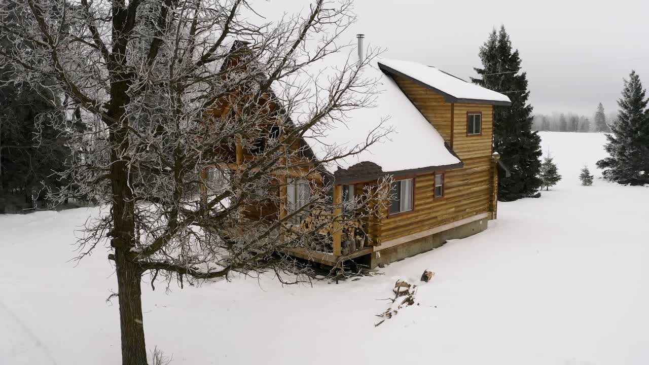 una tranquila y cálida cabaña de troncos de invierno durante una suave nevada con leña sentada en el porche delantero