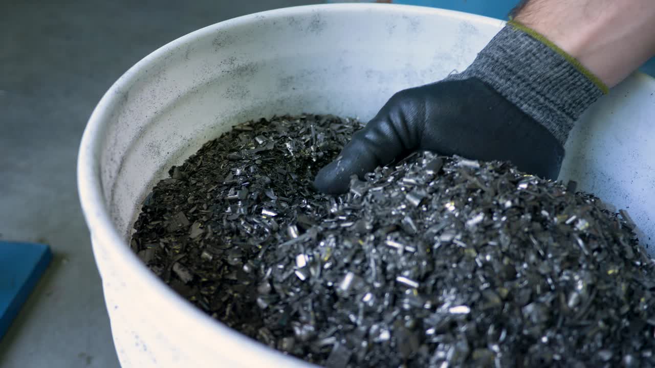 Gloved hand picks up metal flakes at metal recycling plant