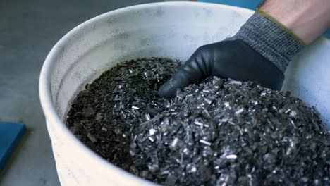 gloved hand picks up metal flakes at metal recycling plant