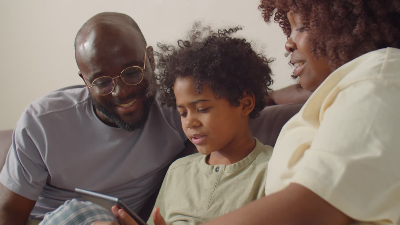 African American Family Sitting on Sofa at Home and Using Tablet