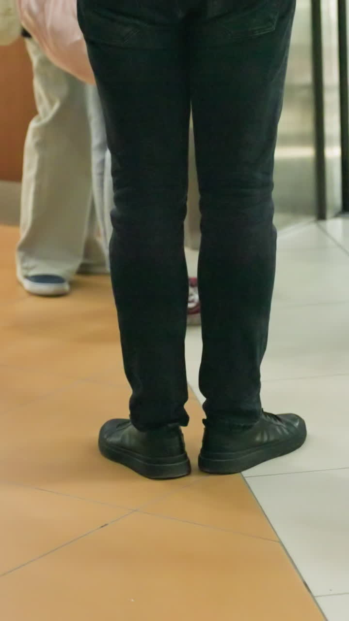 la mitad inferior de varias personas de pie y moviéndose en un centro comercial. la imagen se centra en diferentes piernas y calzado, destacando un ambiente interior ocupado con diversos individuos