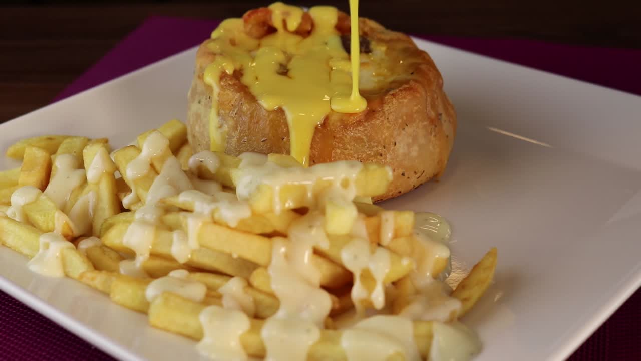 Salsa al formaggio fuso versata su una torta salata e patatine fritte