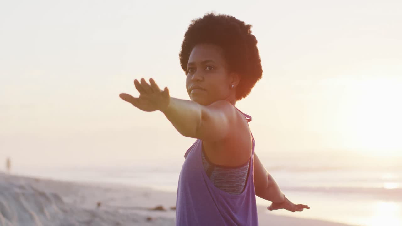 Happy african american woman practicing yoga on sunny beach