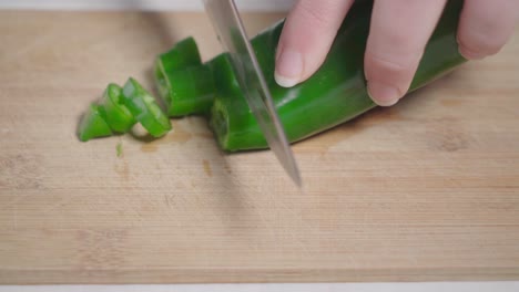 hand slicing green pepper with kitchen knife on wooden cutting board, closeup