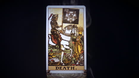 a tarot death card sits on a brass stand as smoke rises around it