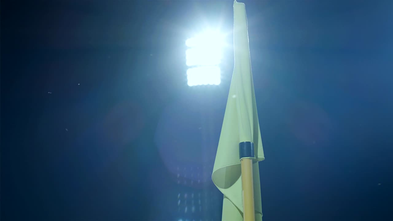 el poste de la bandera de la esquina soplado por el viento en el estadio de fútbol por la noche, las luces del estadio en el fondo