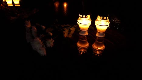 Reflejo-De-Velas-En-Llamas-Con-Flores-En-El-Cementerio,-Ambiente-Nocturno-Oscuro-Alejar