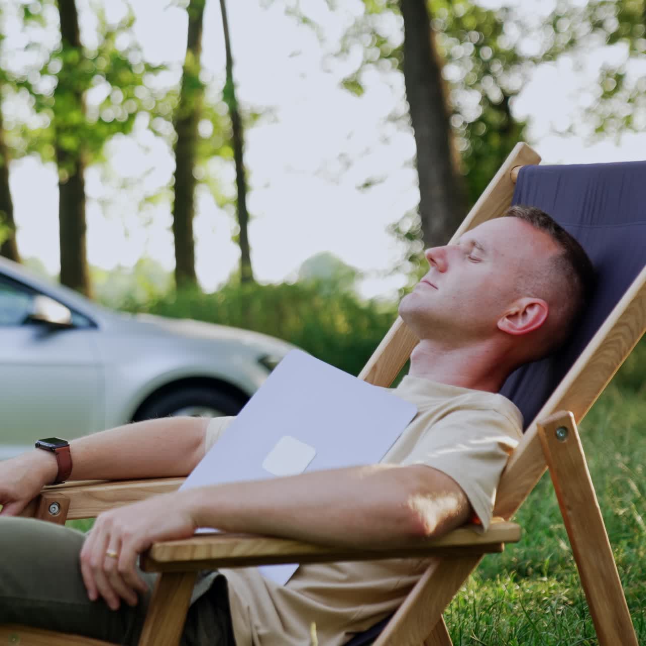 Un libero professionista dorme su una sedia pieghevole con il viso coperto da un portatile. Uomo stanco che si concede una pausa dal lavoro nella natura
