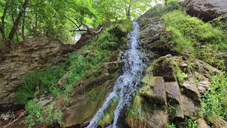 Maries-Waterfall,-Surrounded-By-Lush-Green-Vegetation-And-Rocks-Covered-By-Moss,-Sun-Rays,-Tree,-Thassos-Island,-Greece