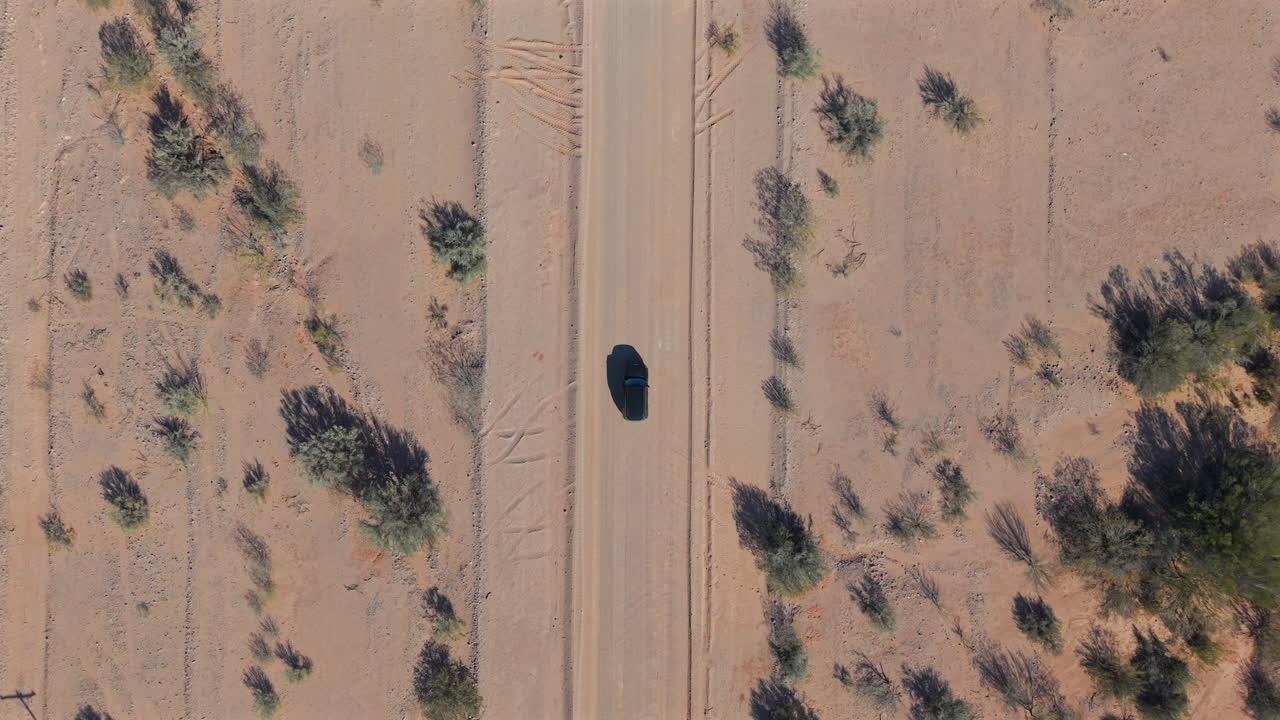 Car driving on remote dirt road, travel and adventure through desert landscape under a bright sun, highlighting the isolation and freedom of off road travel exploration, top down aerial