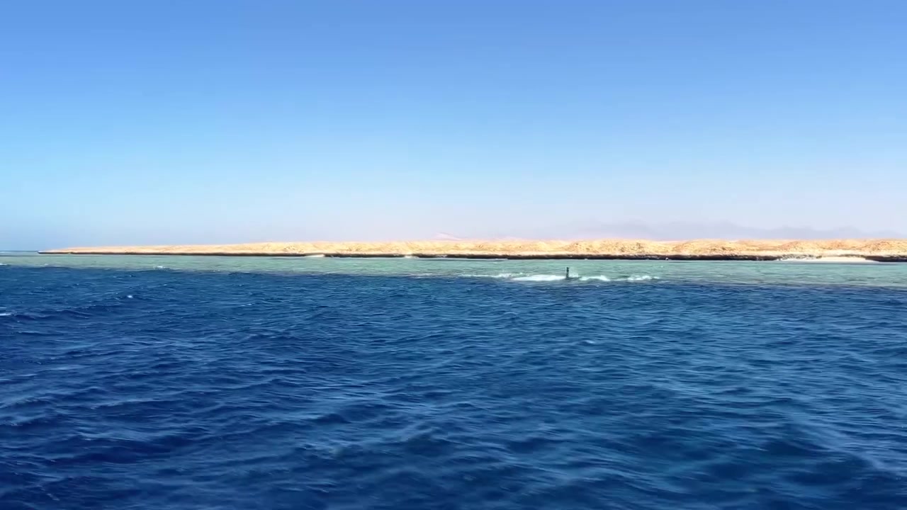 Mısır'da berrak gökyüzü altında, kumlu sahil şeridiyle derin mavi denizde ilerleyen tekne.