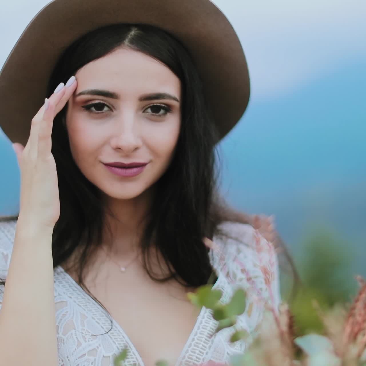 Portrait of brunette girl in nature. Beautiful young woman in hat and sexy dress posing at camera on the blurred nature background.