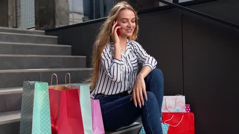 Girl-sitting-on-stairs-with-bags-talking-on-mobile-phone-about-sale-in-shopping-mall-in-Black-Friday