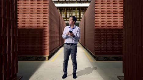 full body of asian male professional worker with his smartphone with red brick packed in stacks are stored, he observes by looking around before he come to concentrating with his smartphone
