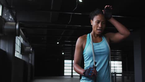 mujer afroamericana cansada después de saltar la cuerda en un edificio urbano vacío