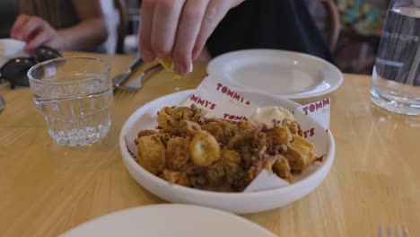 hand squeezing lemon over fried calamari