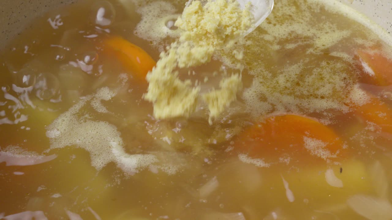Kyllingebouillonpulver tilsat en kogende suppe. Nærbillede i slowmotion