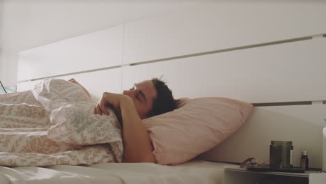 hombre transgénero despertando y usando un teléfono inteligente en el dormitorio