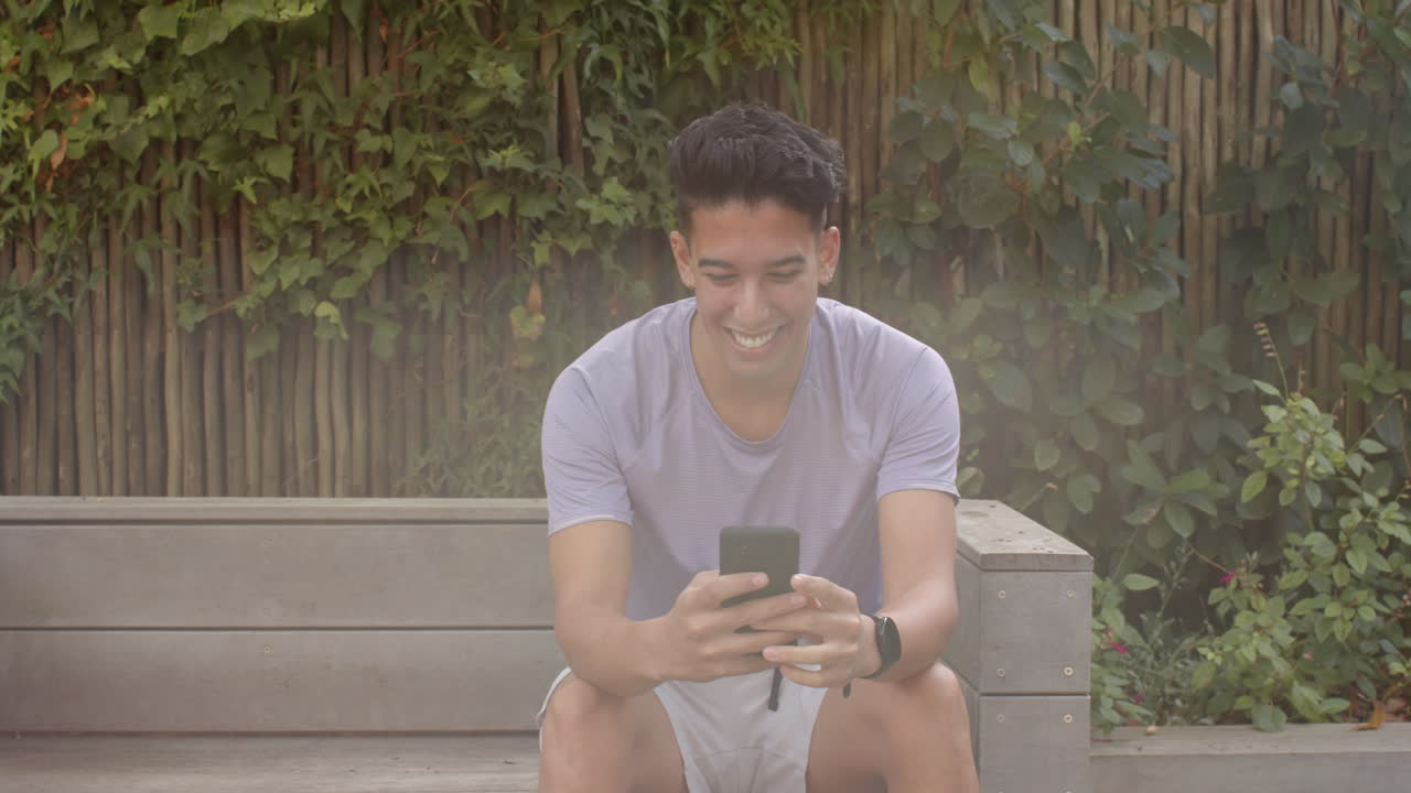 Smiling man sitting on bench, using smartphone, enjoying outdoor time, copy space