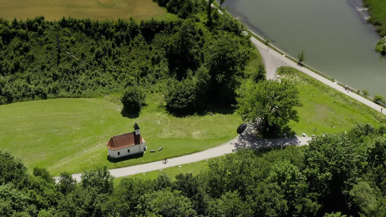 Luftfoto af en lille kirke i grønne omgivelser, mens en sporty cyklist kører forbi på vejen en solrig sommerdag.