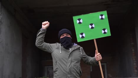 a man wearing a black face mask holds a poster in his hands. copy space tracking points. blank green screen board.