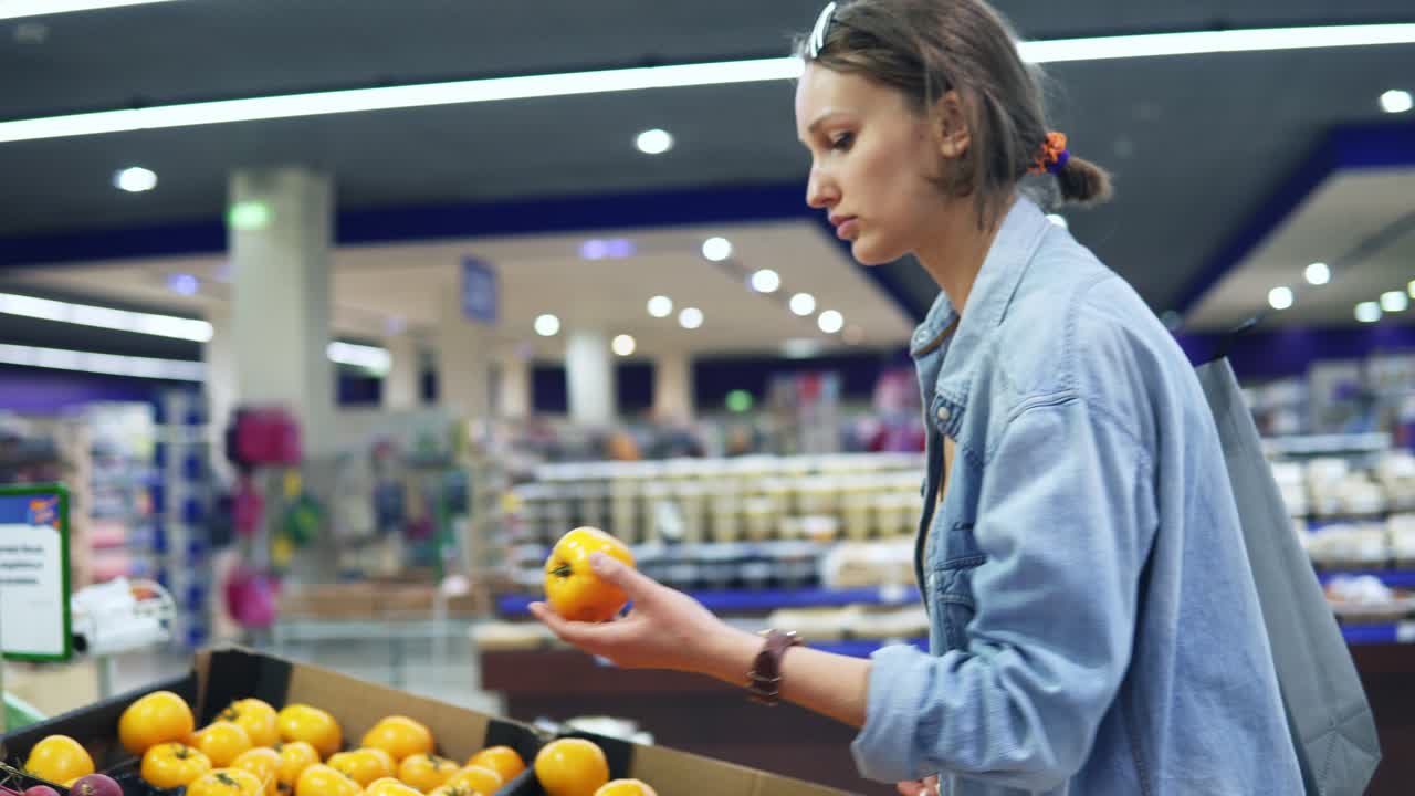 채소 부서의 상자에서 신선한 노란색 토마토를 선택하는 소녀의  ⁇ 드헬드 영상. 식료품 가게. 소녀는 셀로판 가방에 토마토를 추가