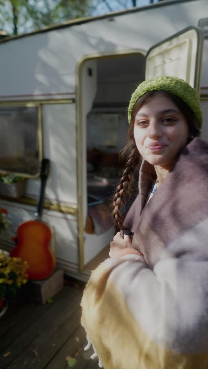 Donna con cappello di lana e coperta vicino a un camper, paesaggio autunnale