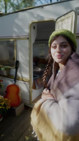 woman in a knitted hat and blanket near a camper, autumn scenery