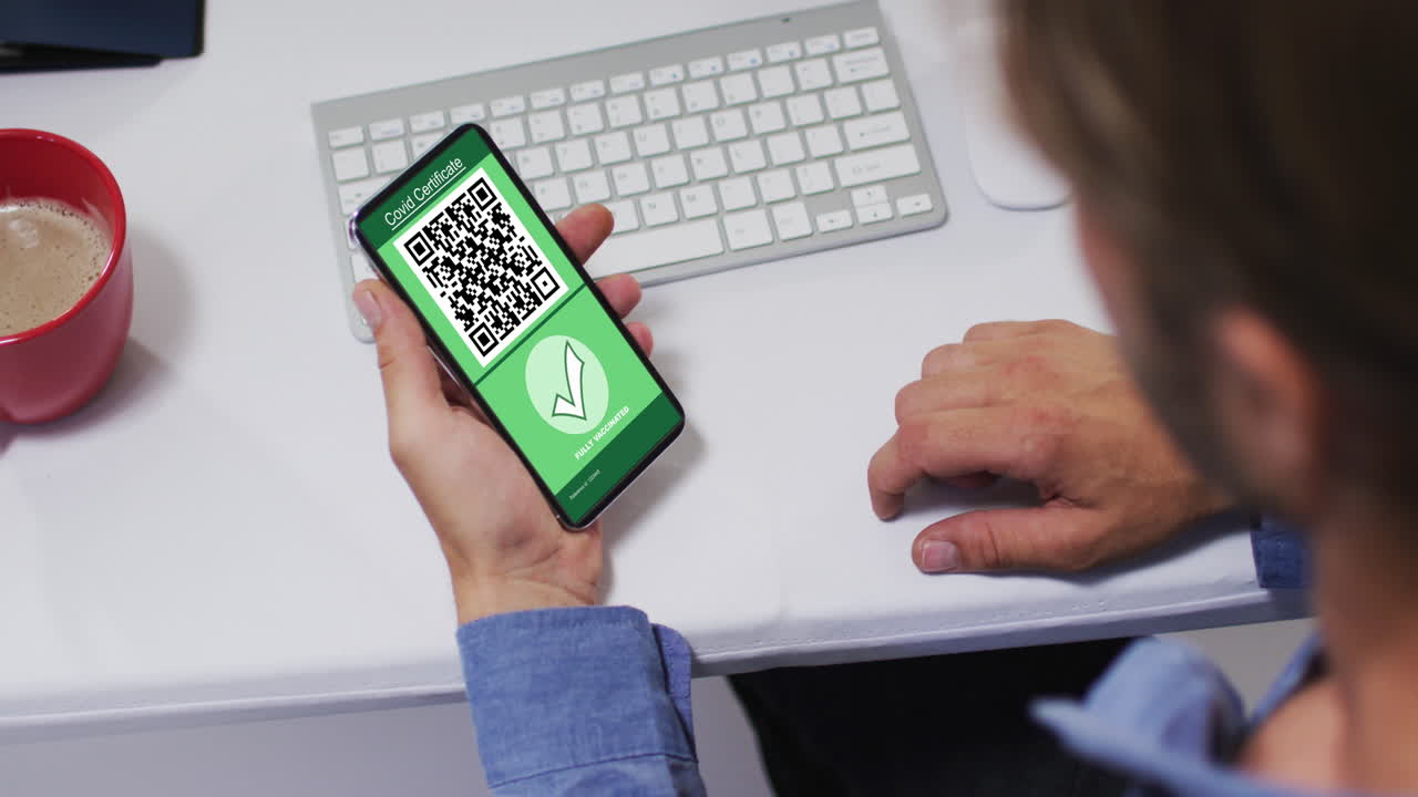 hombre en el escritorio sosteniendo un teléfono inteligente con certificado de vacunación contra la covid y código qr en la pantalla
