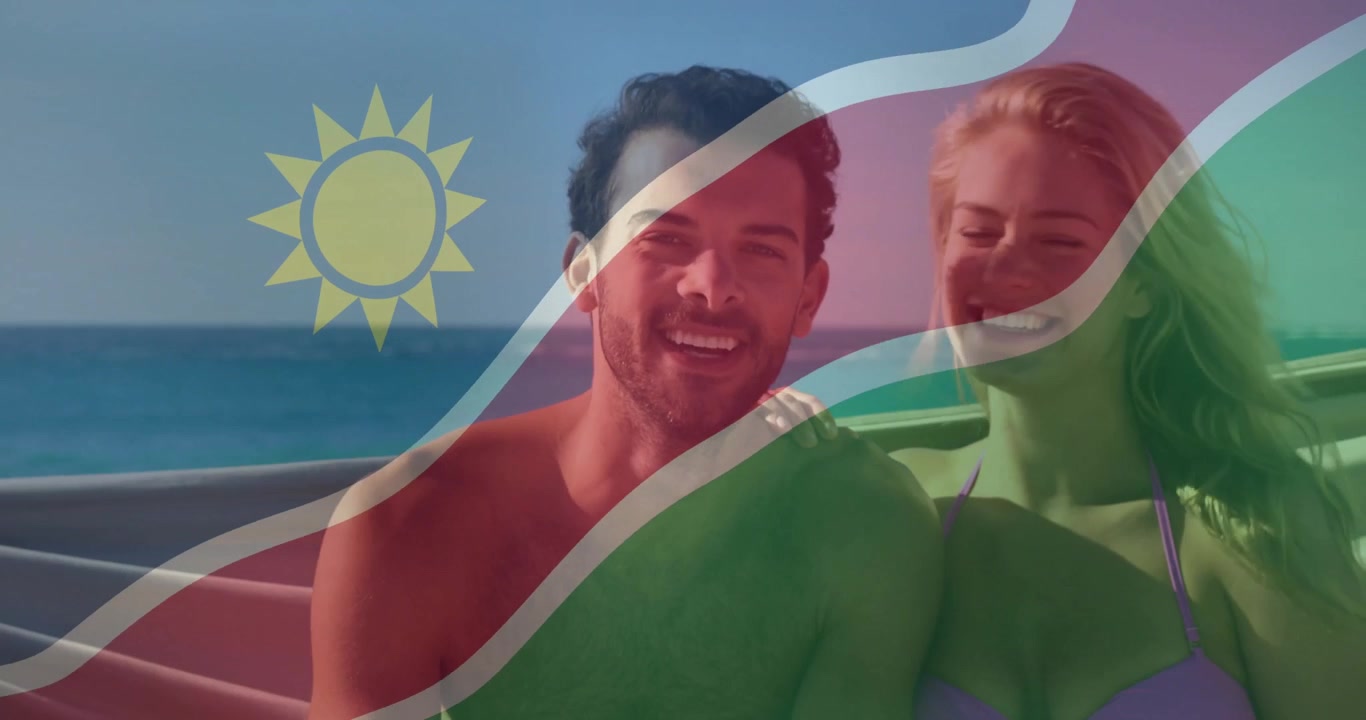 Matkailua mainostava pariskunta, mies kääntyy ja hymyilee istuimella kohti merta, Namibian lipun ollessa päällekkäin