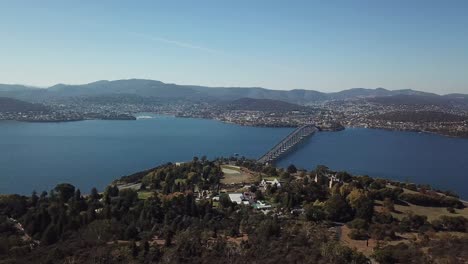 Slow-aerial-pan-over-wide-river-with-vehicular-bridge-and-cityscape-in-Hobart,-Tasmania,-Australia