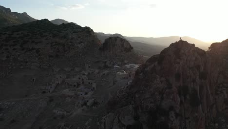 toma aérea moviéndose hacia la derecha y hacia atrás sobre el pequeño pueblo antiguo en ruinas, junto a una empinada montaña rocosa en la hermosa y cálida puesta de sol en túnez