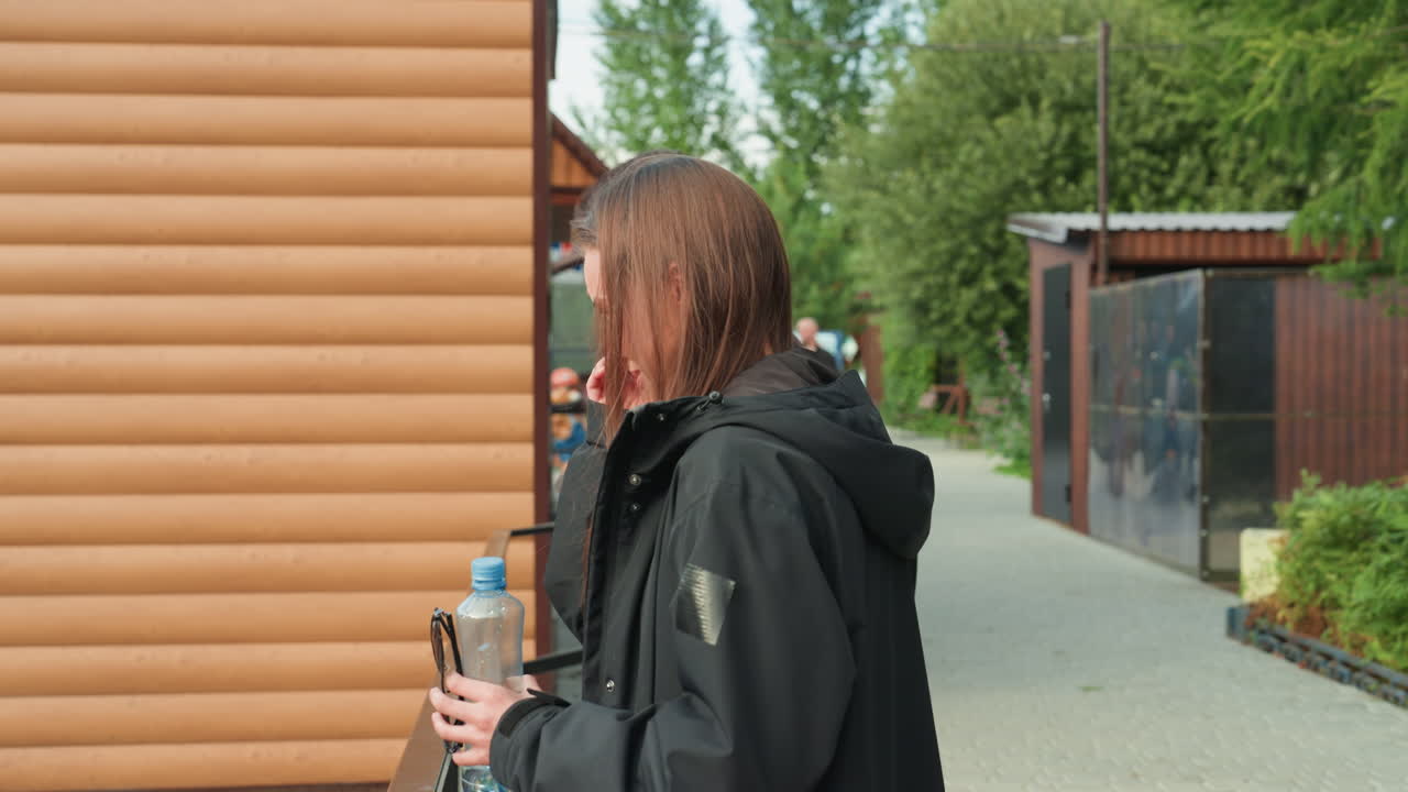 Nuoret valkoihoiset opiskelijat keskustelevat mökin ulkopuolella aurinkoisella lähiöpolulla reppuineen ja pulloineen, nauraen ja jutellen kävellessään puisen sivuraiteen ja kasvillisuuden ohi. Aitoa ja ystävällistä vuorovaikutusta rennosti.