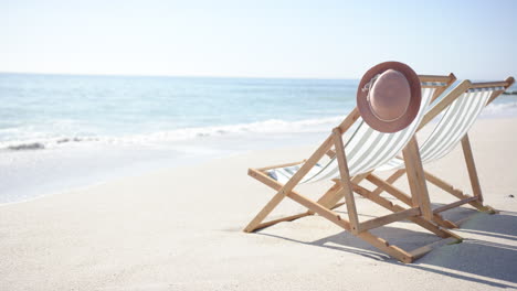 a single deck chair with green and white stripes and a brown hat rests on a sandy beach with copy sp