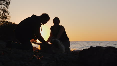 hombre y mujer jugando con perro al atardecer